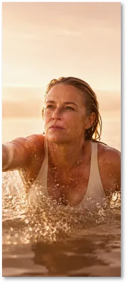 A woman swimming in open water, reaching forward through the light